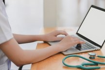 Image du m&eacute;decin en train de travailler sur son ordinateur portable avec son st&eacute;thoscope pos&eacute; &agrave; c&ocirc;t&eacute;